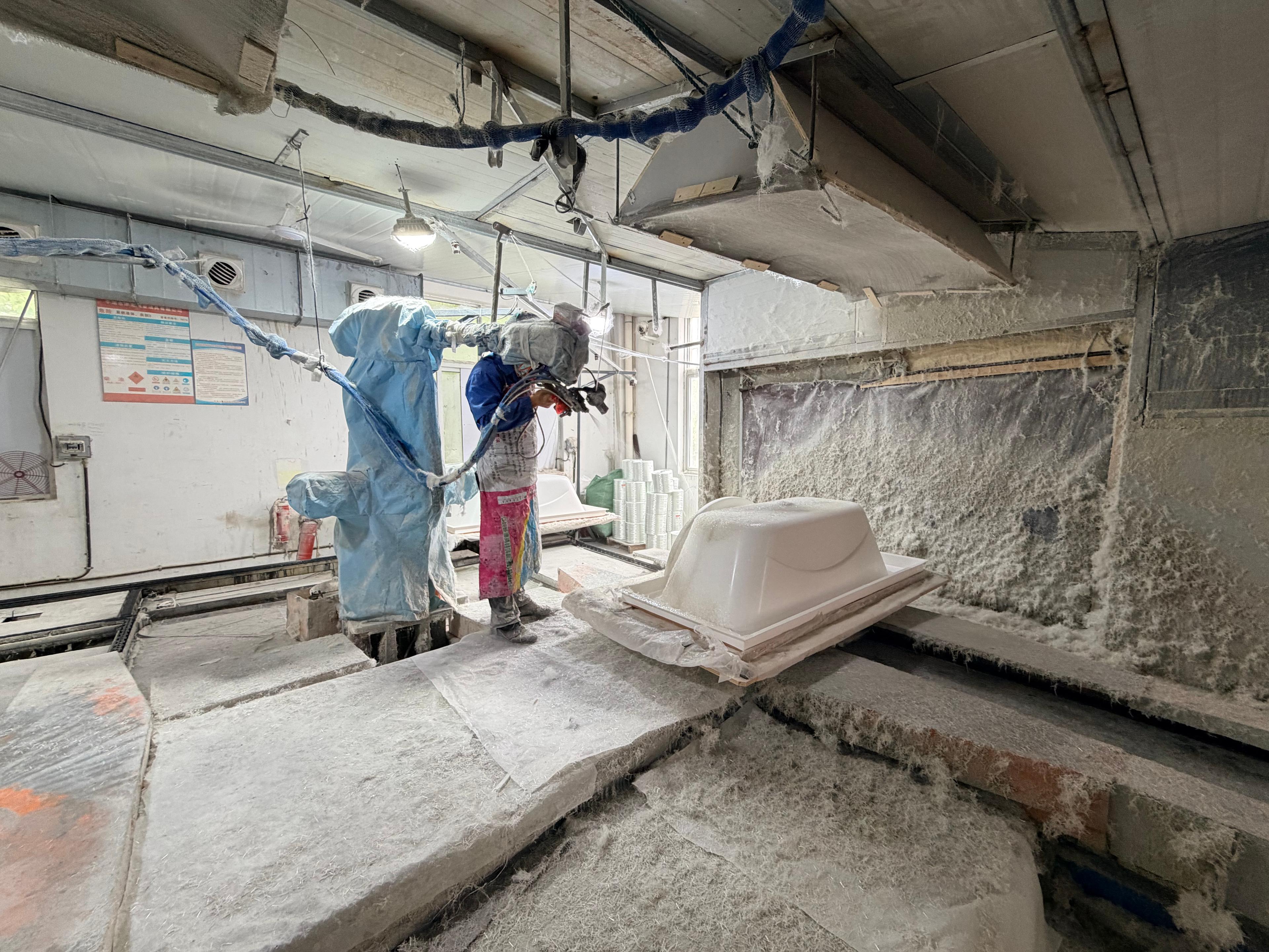 Workers applying fiberglass reinforcement to a bathtub shell